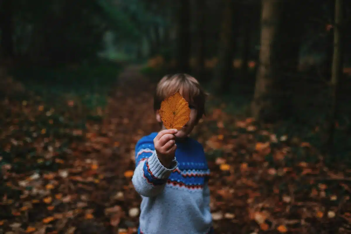 Enfant qui cache son visage derrière une feuille, comme derrière un masque